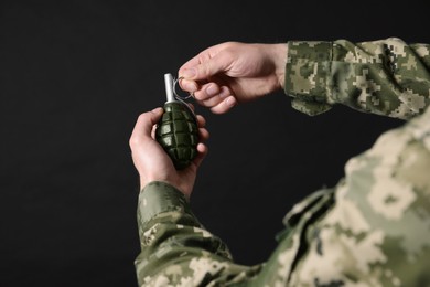 Soldier pulling safety pin out of hand grenade on black background, closeup. Military service