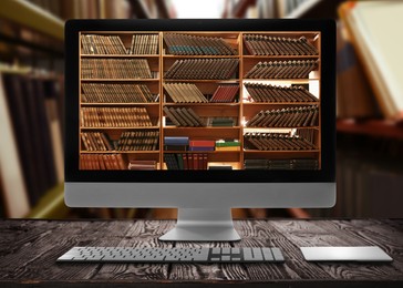 Image of Online library. Modern computer on wooden table and shelves with books indoors