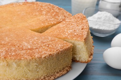 Tasty sponge cake and ingredients on light blue wooden table, closeup