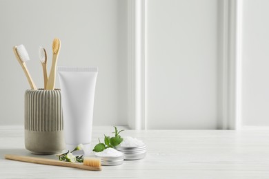 Toothbrushes, toothpaste and herbs on white wooden table. Space for text