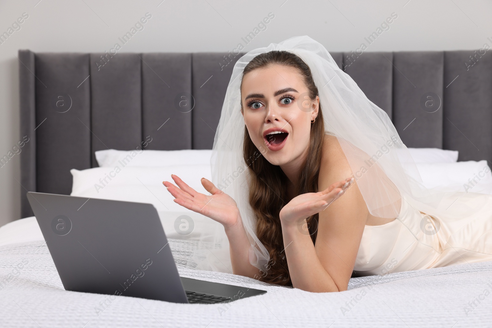 Photo of Shocked bride with laptop on bed in bedroom