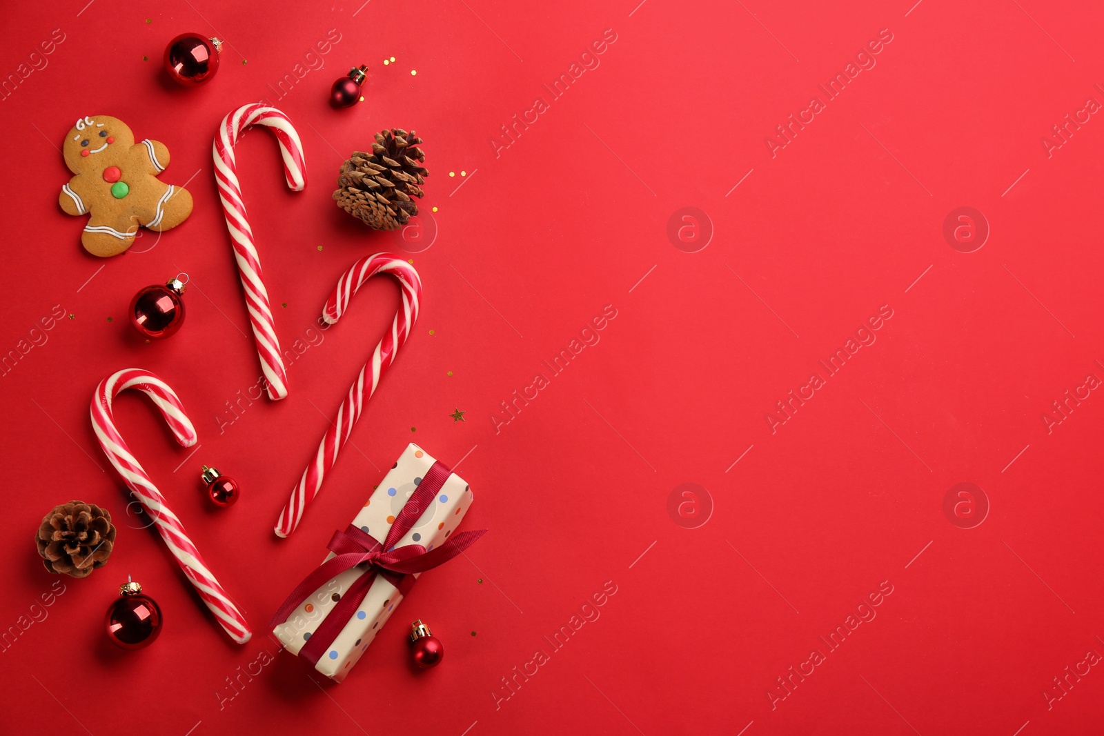 Photo of Flat lay composition with candy canes and Christmas decor on red background. Space for text