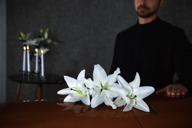 Photo of Young man near casket with white lilies in funeral home