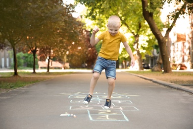 Photo of Little child playing hopscotch drawn with colorful chalk on asphalt
