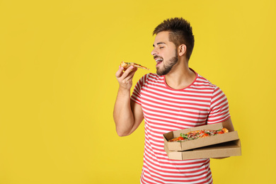 Handsome man eating tasty pizza on yellow background