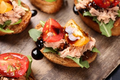 Photo of Delicious bruschetta with balsamic vinegar, tomato, arugula and tuna on wooden table, closeup