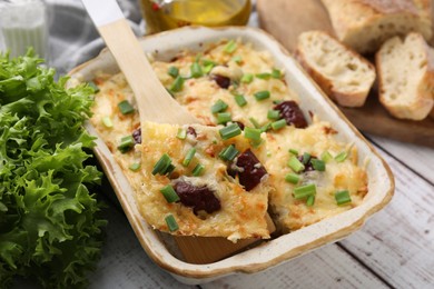 Photo of Taking piece of tasty sausage casserole from baking dish at white wooden table, closeup