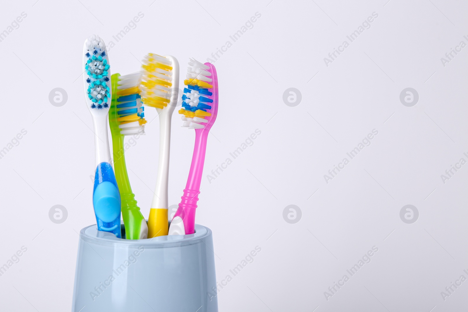 Photo of Different toothbrushes in holder on light grey background, closeup. Space for text