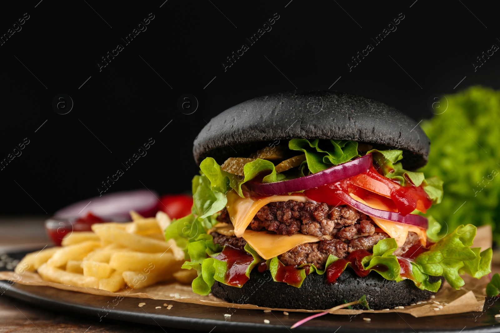 Photo of Plate with black burger and French fries on table. Space for text