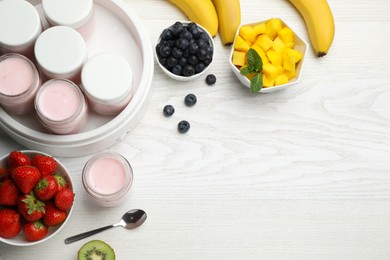 Photo of Yogurt maker with jars and different fruits on white wooden table, flat lay. Space for text