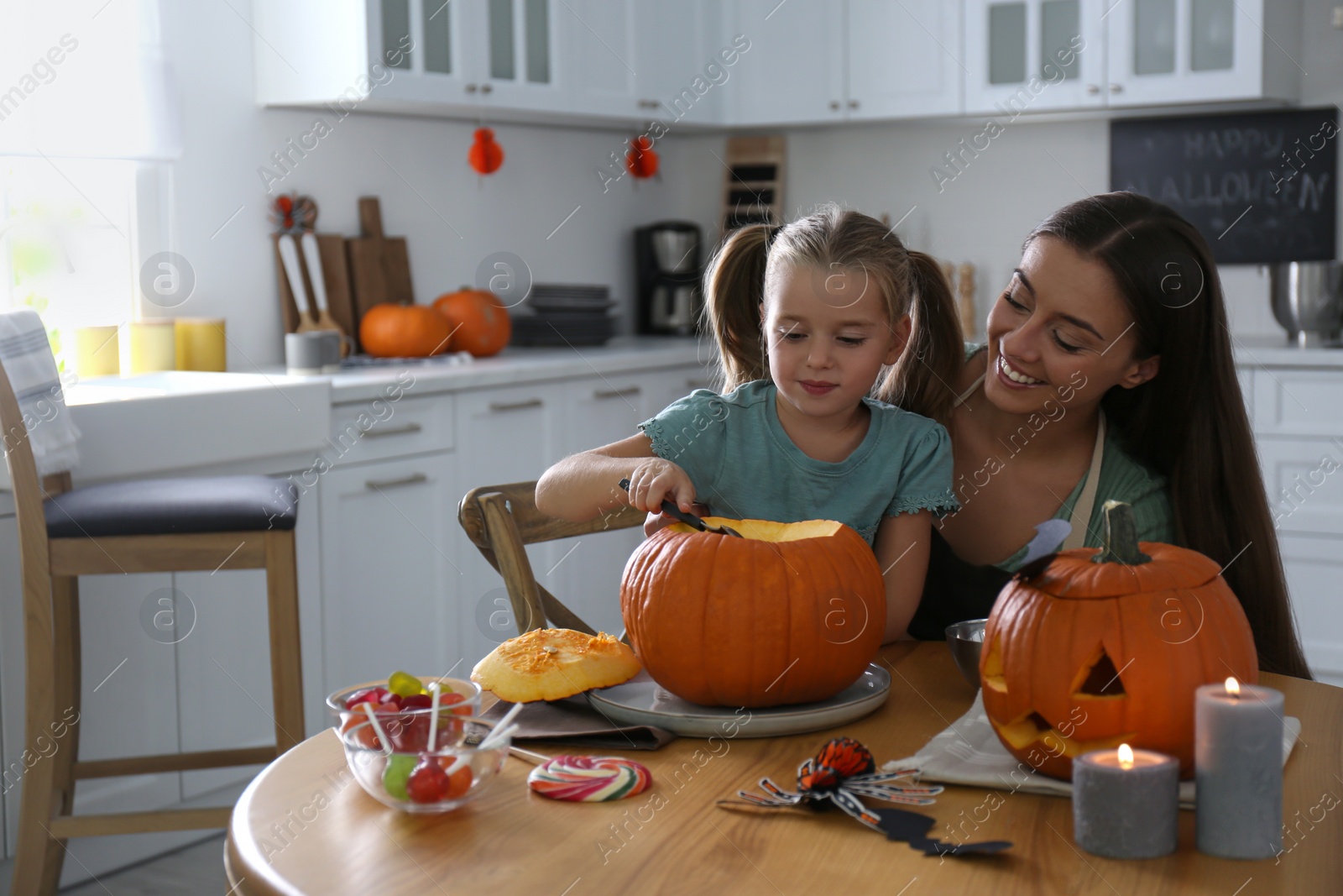 Photo of Mother and daughter making pumpkin jack o'lantern at table in kitchen. Halloween celebration