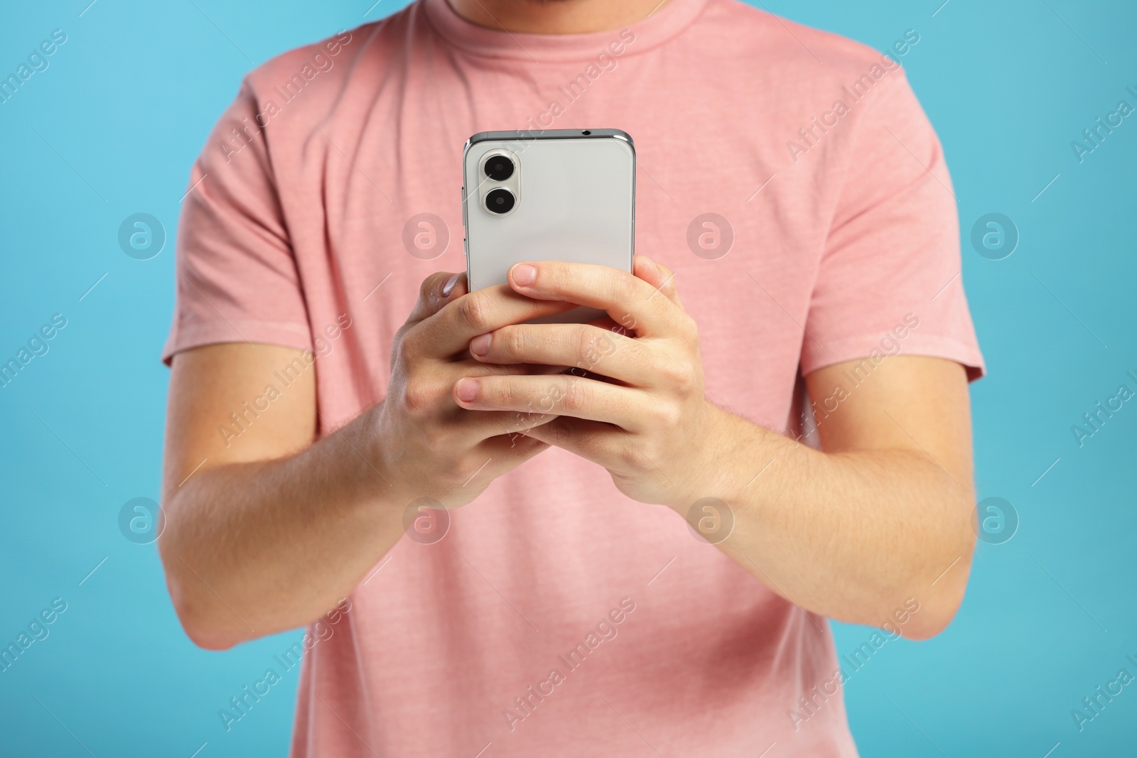 Photo of Man sending message via smartphone on light blue background, closeup