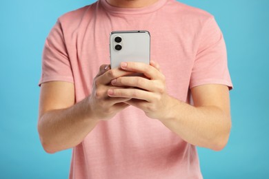 Man sending message via smartphone on light blue background, closeup