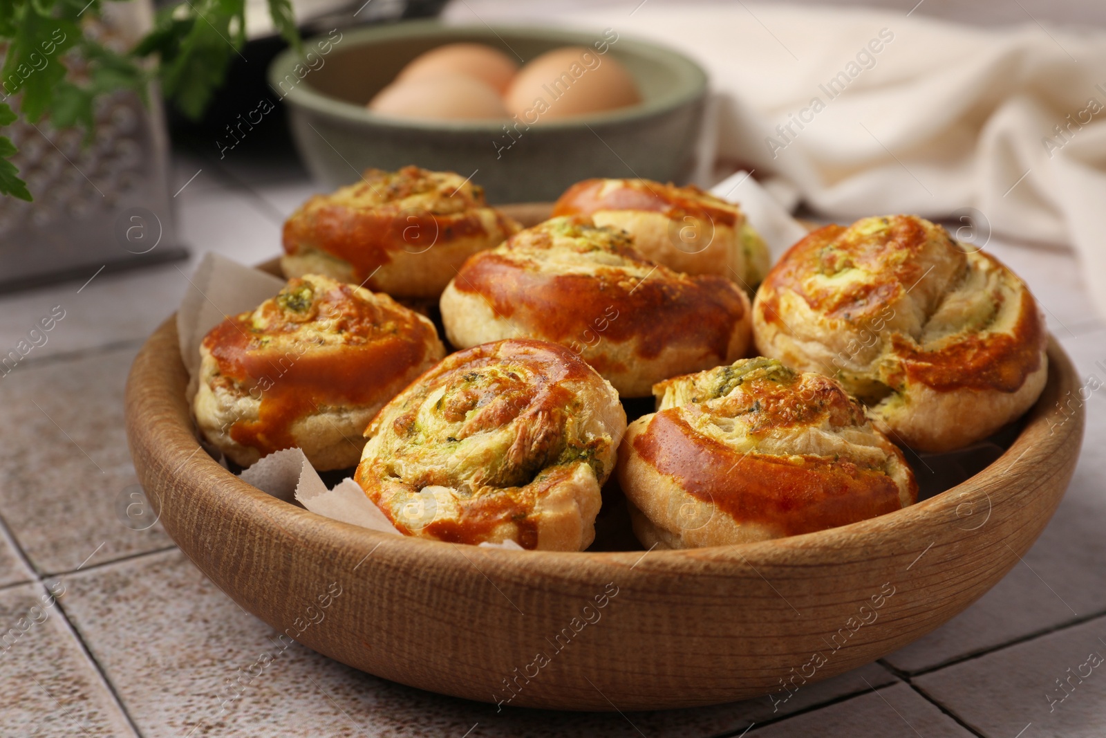 Photo of Fresh delicious puff pastry with tasty filling in wooden bowl on white tiled surface, closeup