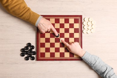 Photo of Senior man playing checkers with woman at white wooden table, top view