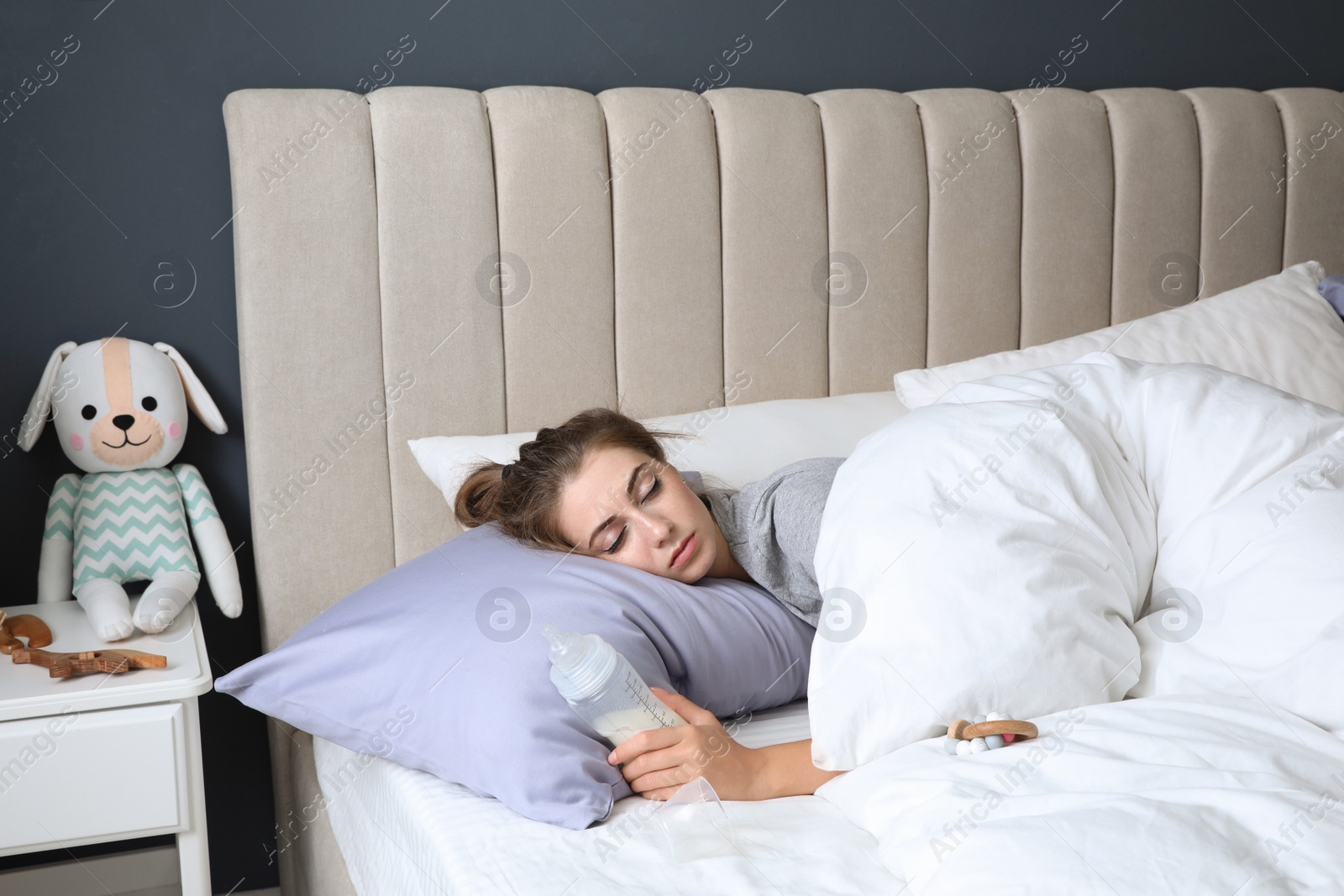 Photo of Exhausted young mother with bottle of milk sleeping in bed at home