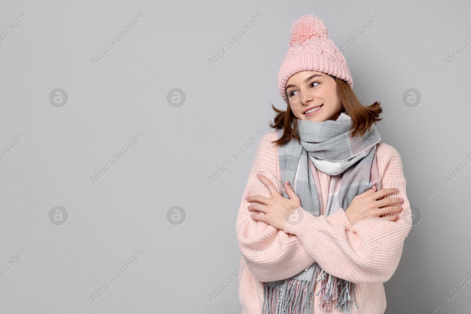 Photo of Beautiful woman in warm scarf and hat on gray background, space for text