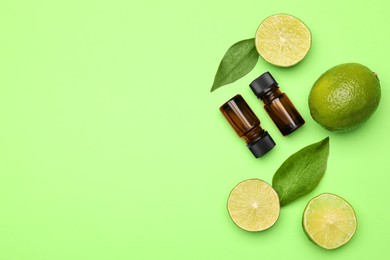 Photo of Bottles of citrus essential oil and fresh limes on green background, flat lay. Space for text