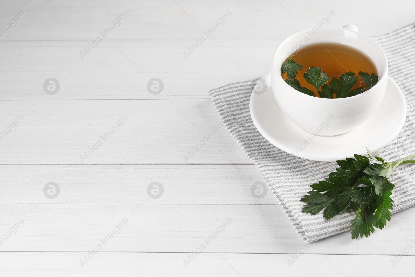 Photo of Aromatic herbal tea and fresh parsley on white wooden table, space for text