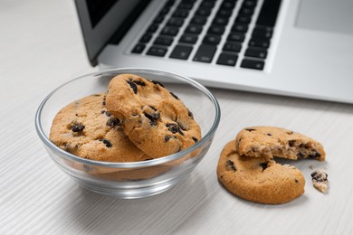 Photo of Chocolate chip cookies and laptop on white wooden table, closeup
