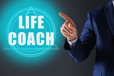 Image of Personal development concept. Businessman pointing at virtual screen with text Life Coach on dark background, closeup