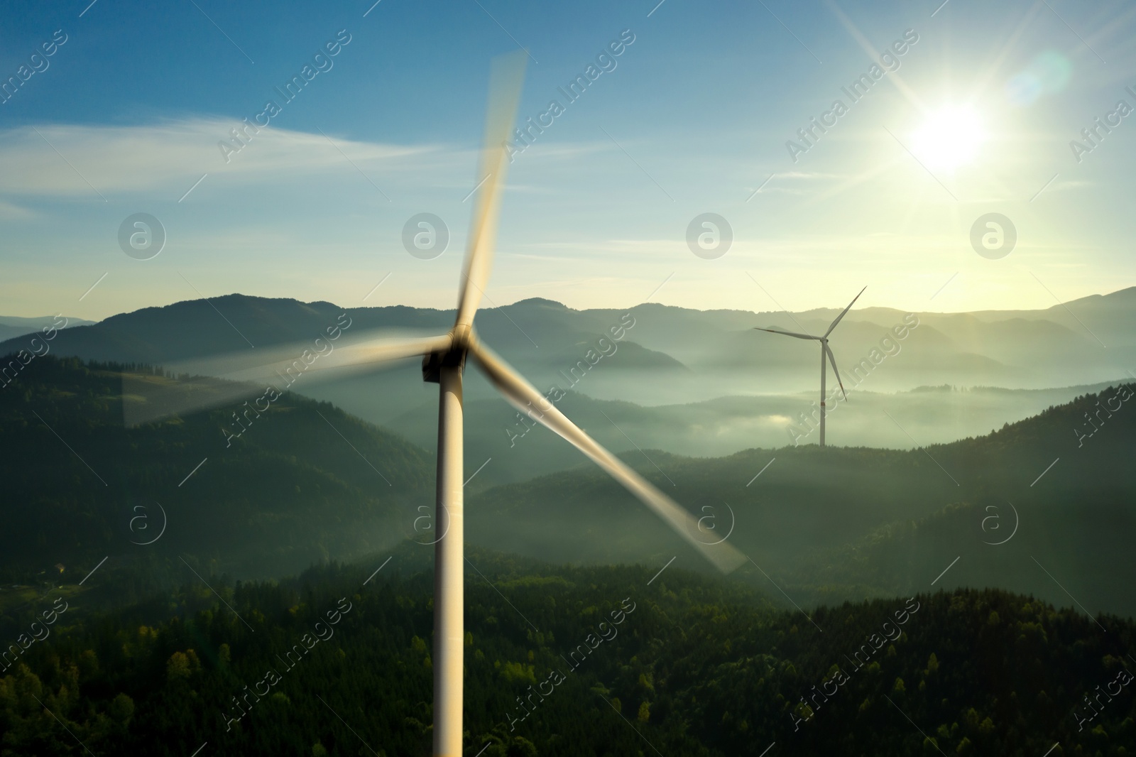 Image of Modern wind turbines in mountains on sunny day. Alternative energy source