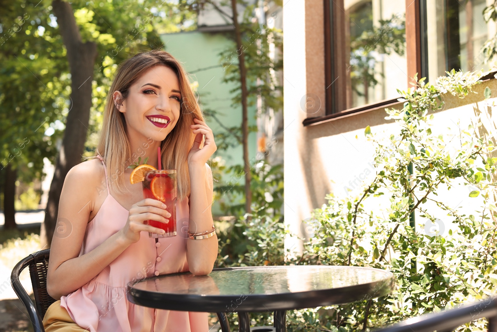 Photo of Young woman with glass of tasty lemonade at table in cafe, outdoors. Natural detox drink