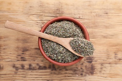 Photo of Bowl and spoon with dried thyme on wooden table, top view