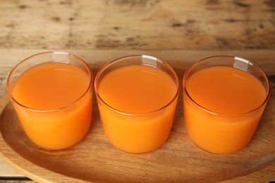 Photo of Glasses of freshly made carrot juice on wooden plate