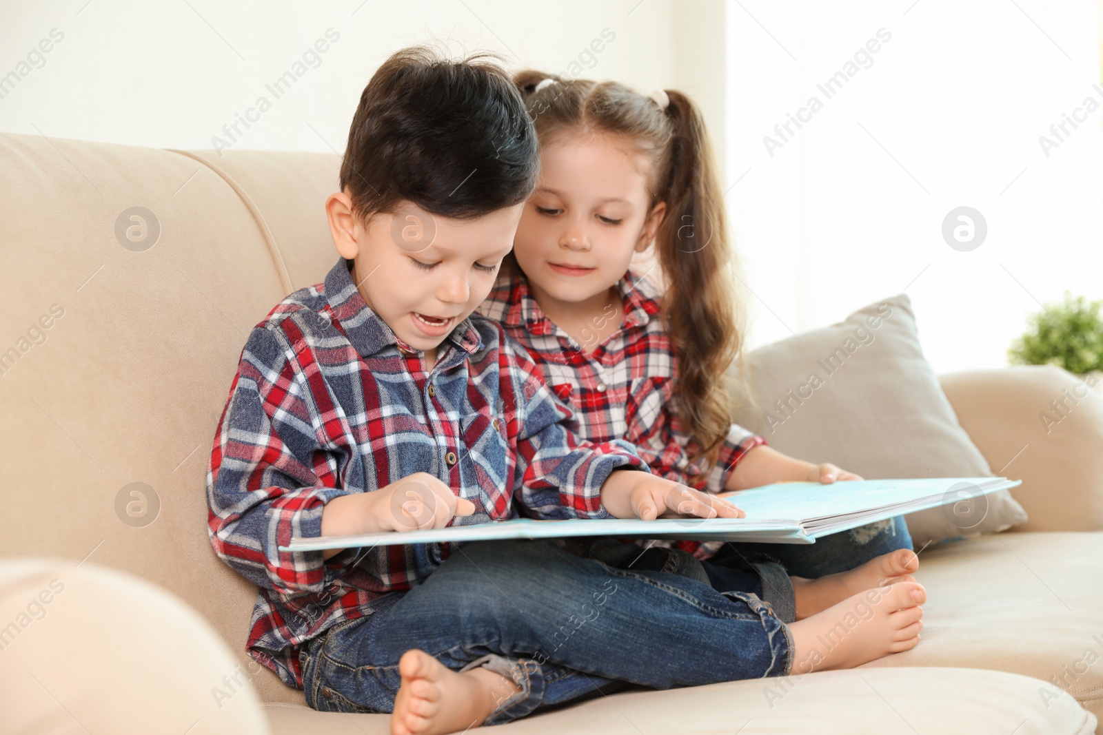 Photo of Cute children reading book on sofa in living room