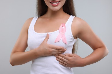 Photo of Woman with pink ribbon on light grey background, closeup. Breast cancer awareness