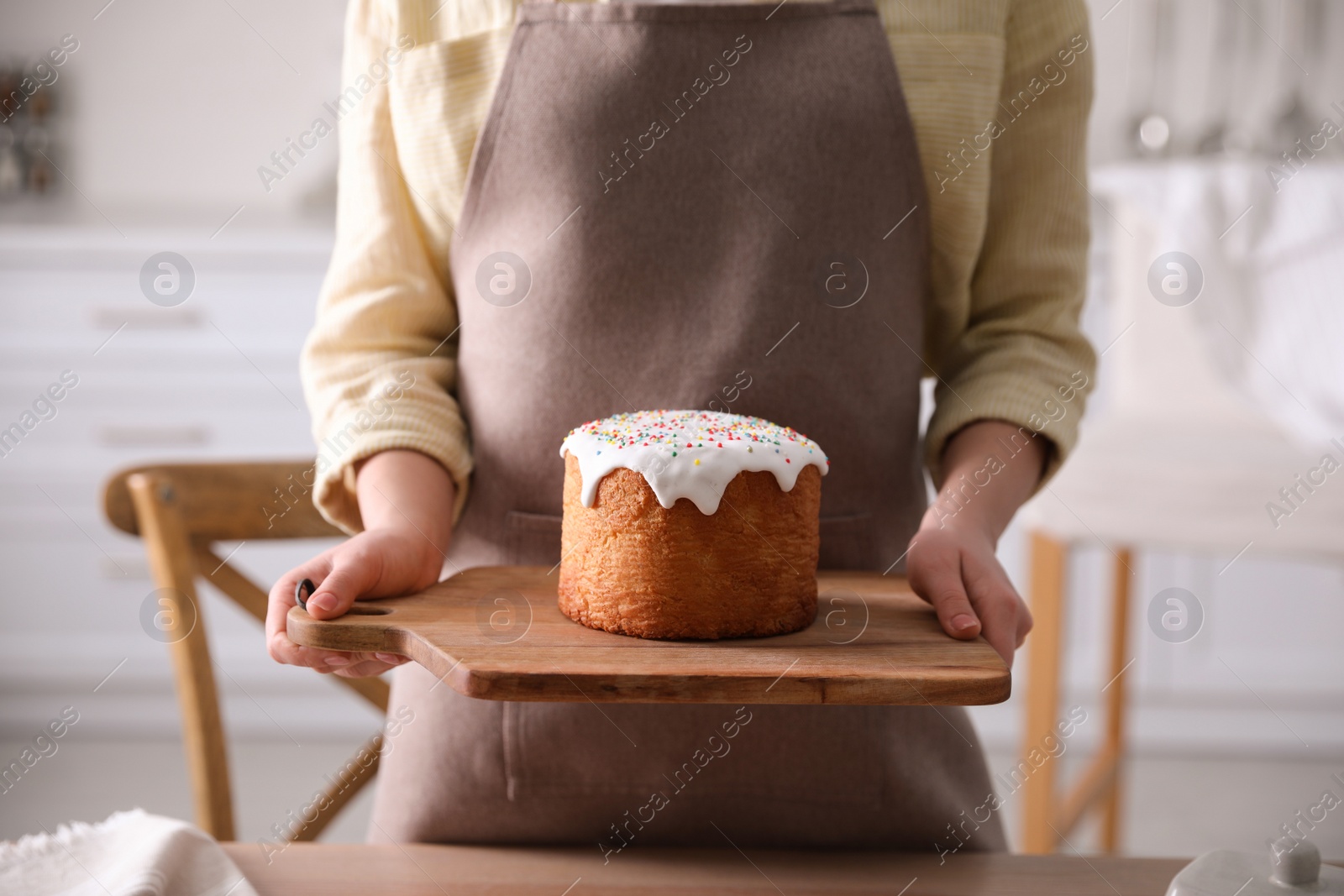 Photo of Young woman holding board with traditional Easter cake in kitchen, closeup