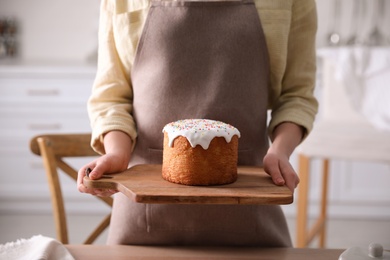 Young woman holding board with traditional Easter cake in kitchen, closeup