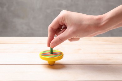 Photo of Woman playing with bright spinning top at light wooden table, closeup