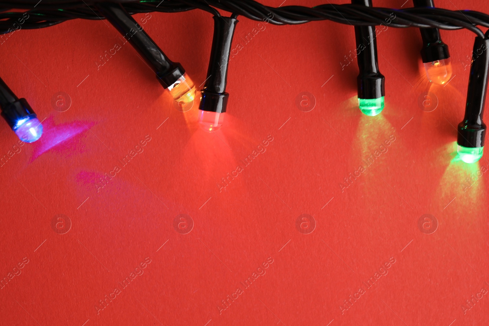 Photo of Glowing Christmas lights on color background, closeup