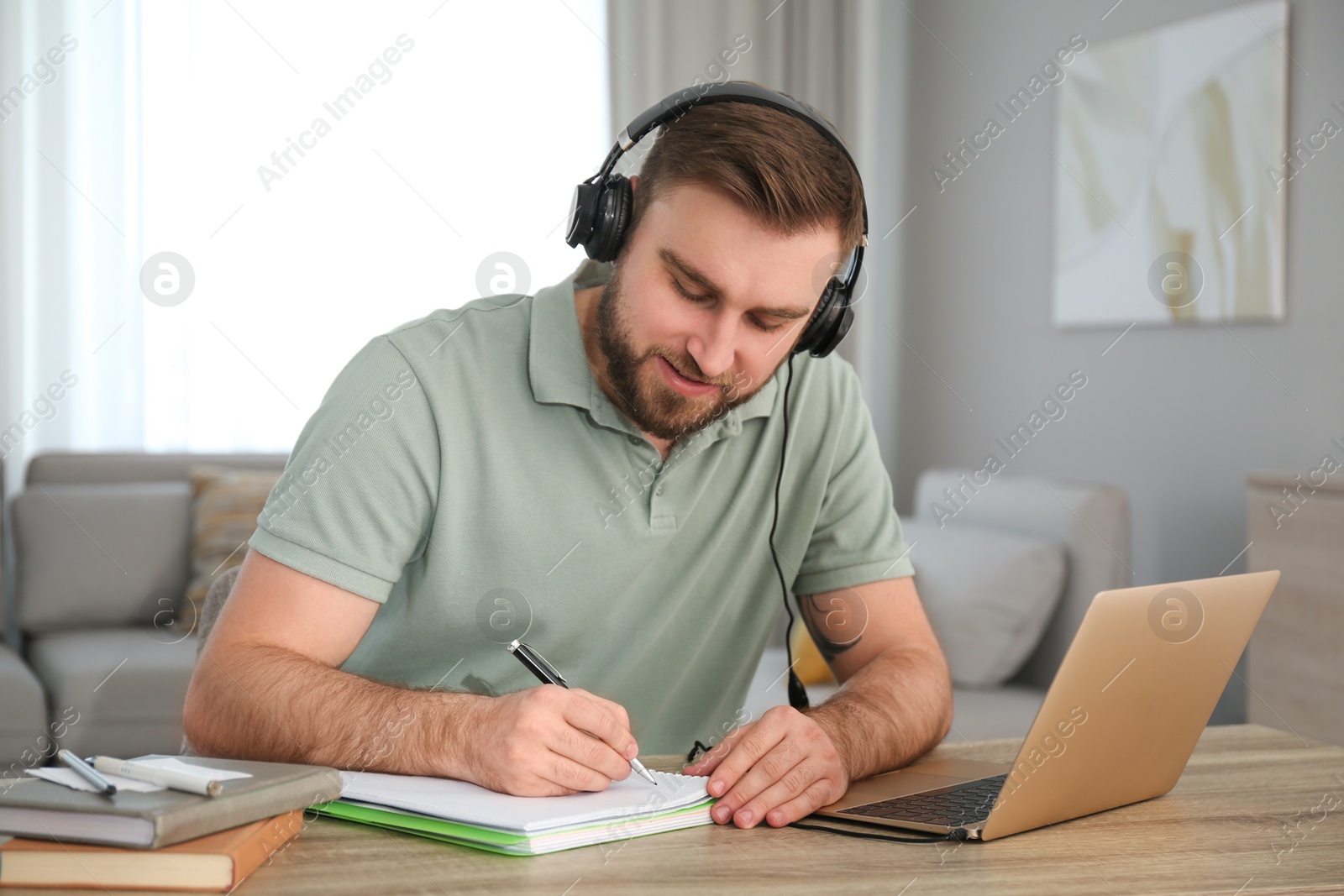 Photo of Young man taking notes during online webinar at table indoors