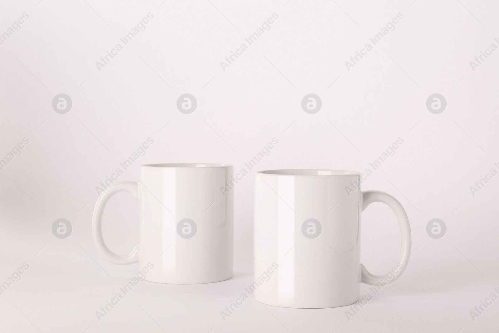 Blank white ceramic mugs on light background Photo of Blank white ceramic mugs on light background