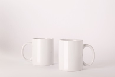 Photo of Blank white ceramic mugs on light background
