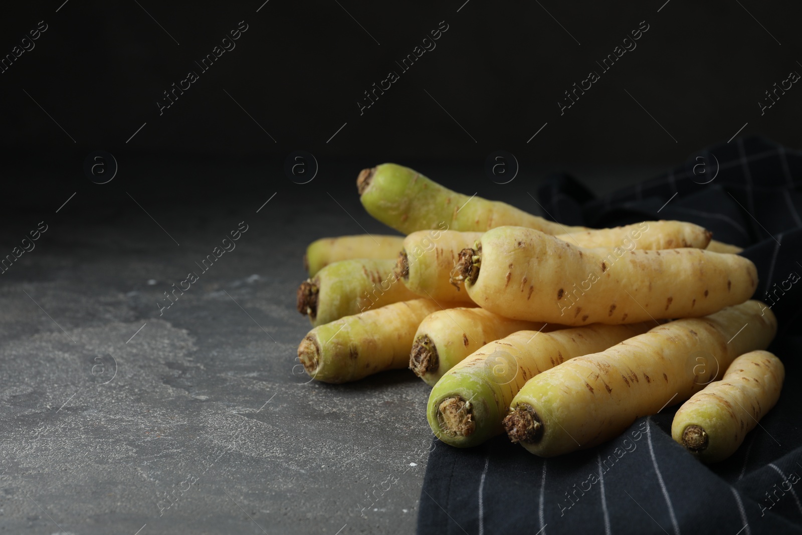 Photo of Raw white carrots on grey table against black background. Space for text