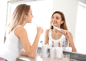 Photo of Young beautiful woman with toothbrush near mirror in bathroom. Personal hygiene