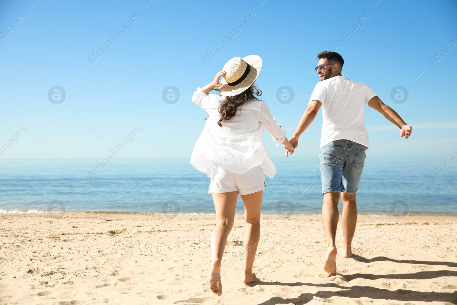 Photo of Young couple running on beach near sea. Honeymoon trip