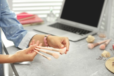 Photo of Young beauty blogger with brushes at light grey marble table, closeup