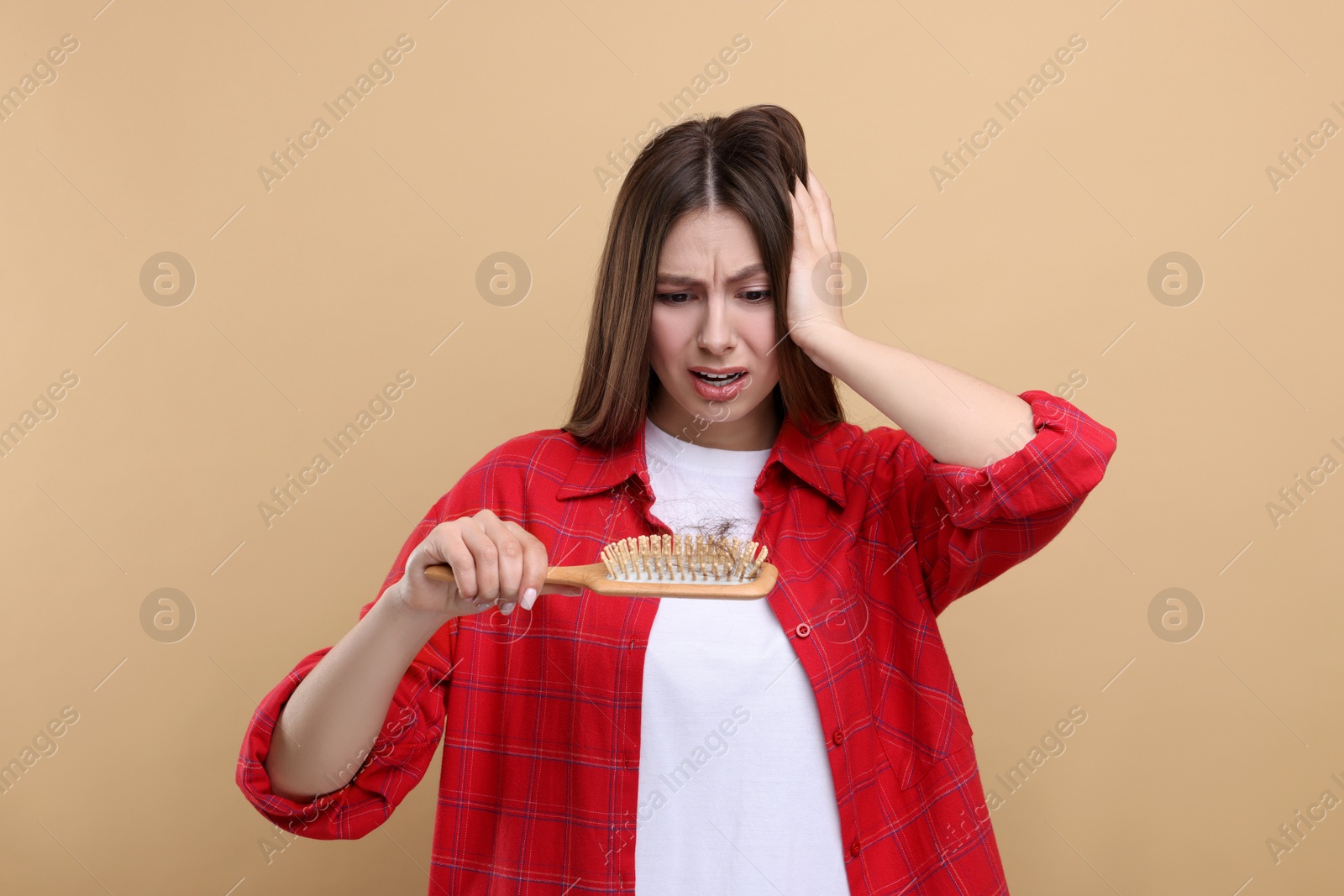 Photo of Emotional woman holding brush with lost hair on beige background. Alopecia problem