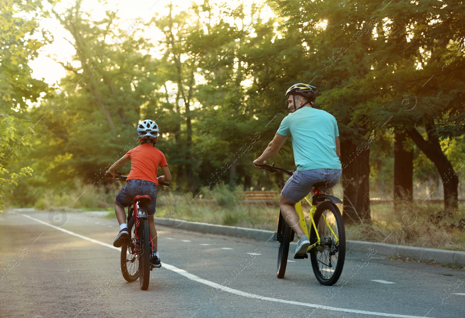 Photo of Dad and son riding bicycles in park on sunny day