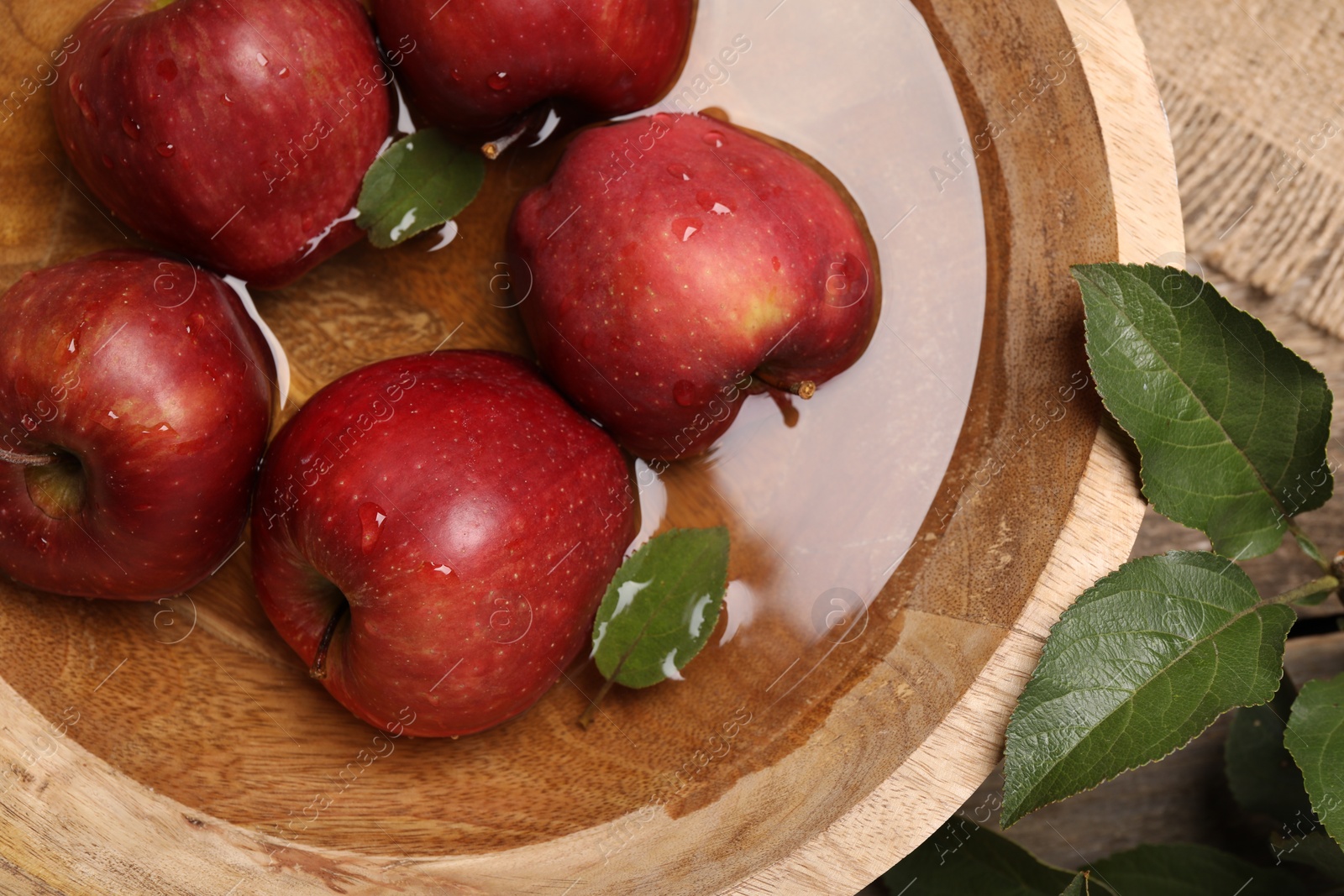 Photo of Fresh red apples in bowl with water and leaves on table, flat lay