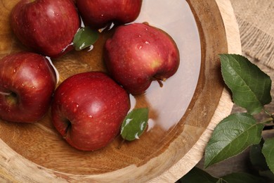Photo of Fresh red apples in bowl with water and leaves on table, flat lay