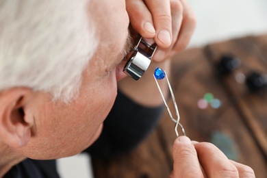 Photo of Male jeweler evaluating precious gemstone in workshop, closeup