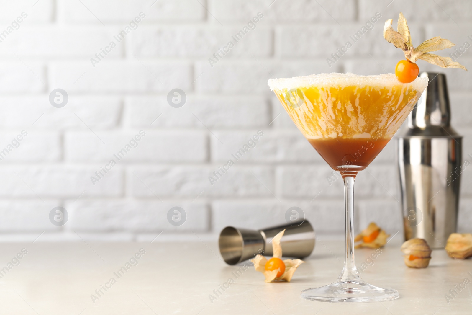 Photo of Delicious cocktail decorated with physalis fruit on light table near white brick wall. Space for text