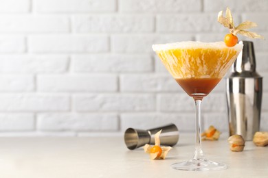 Delicious cocktail decorated with physalis fruit on light table near white brick wall. Space for text