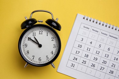 Photo of Alarm clock and calendar on yellow background, flat lay. Reminder concept